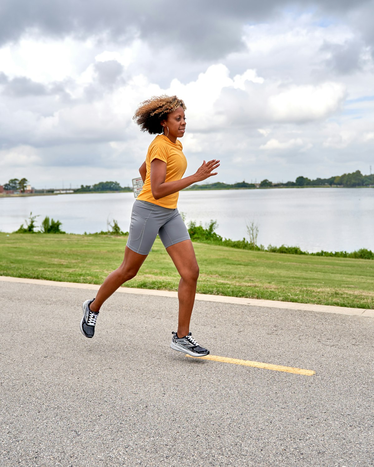 A woman running along a paved path next to a lake on an overcast day